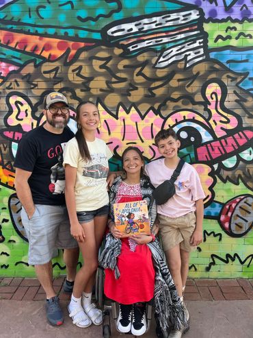 Patty and her family posing for a picture with a colorful mural in the background