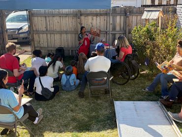 Patty in background reading with group of people on grass in the foreground