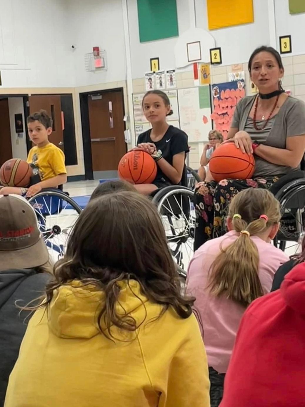 Patty speaking to a group of kids. Her kids are sitting in wheelchairs with basketballs on their lap