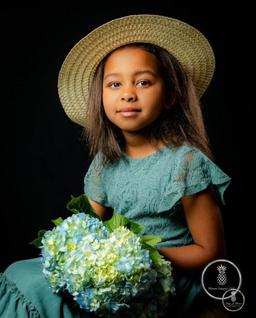 Fine Art Portrait Mount Pleasant SC. Black backdrop. Girl in blue dress, hat, holds hydrangeas