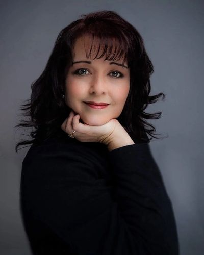 Portrait of a smiling woman with dark hair resting her chin on her hand.