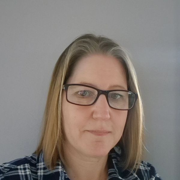 Woman with glasses and shoulder-length hair in a plaid shirt.