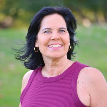 Smiling woman outdoors in a purple sleeveless top.