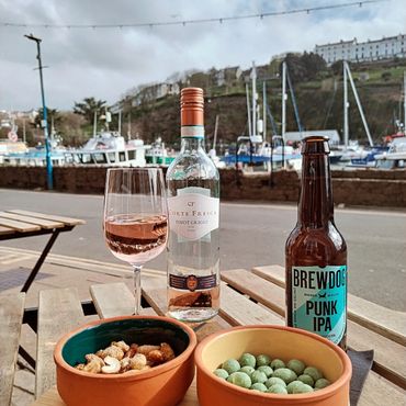 Outdoor table with wine, beer, and snacks by a marina.