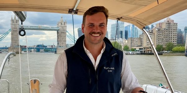 Man smiling on a boat with Tower Bridge in the background.