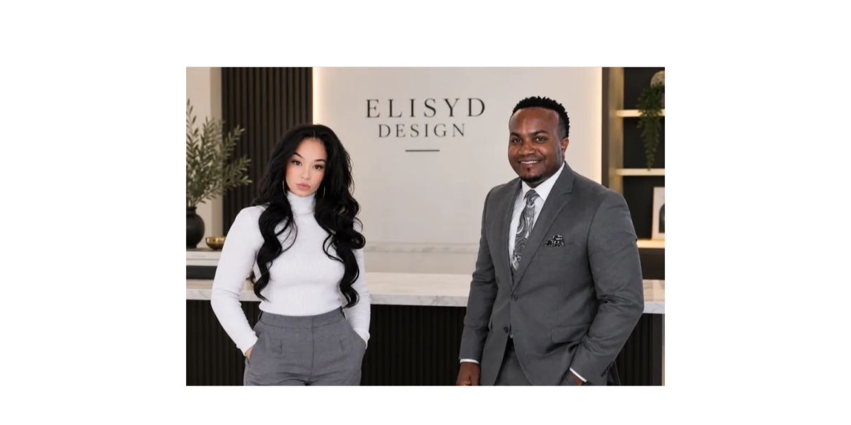 Two professionals posing in an office setting with a design company sign.