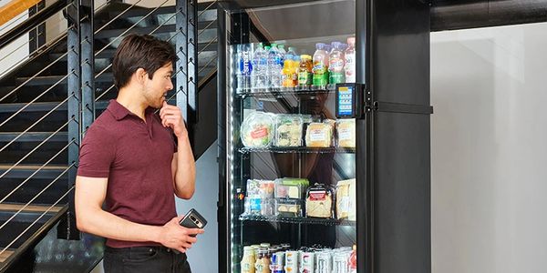 A man looking thoughtfully at a vending machine with various drinks and snacks.