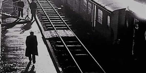 A lone man walking along a train platform in the dark, circa 1940