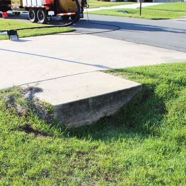 Concrete slab with erosion underneath in a grassy area near a street.