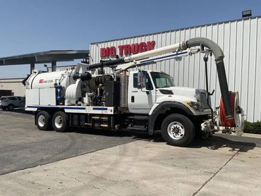White industrial vacuum truck parked outside a building labeled 'BIG TRUCK'.