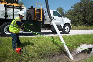 Worker uses vacuum truck to clean a roadside drain.