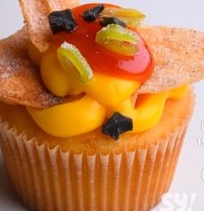 Cupcake topped with vibrant yellow and red frosting, garnished with green and black pieces.
