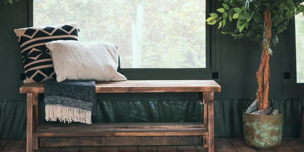 Cozy wooden bench with cushions and a throw, next to a potted plant indoors.