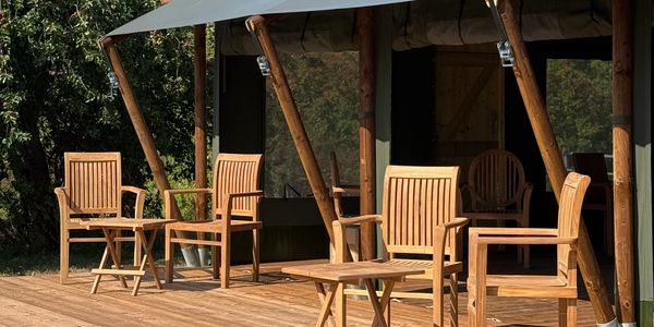 Wooden chairs and tables on a deck outside a canvas tent under a clear blue sky.
