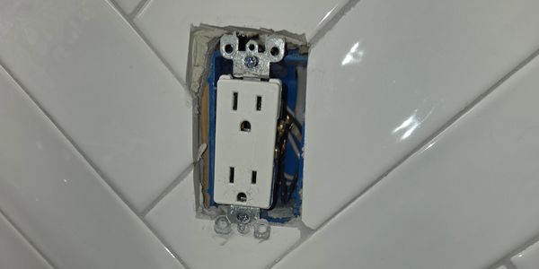 Wall outlet installed in a tiled wall, missing cover plate.