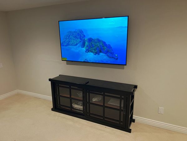 Wall-mounted TV above a black cabinet in a bare room.