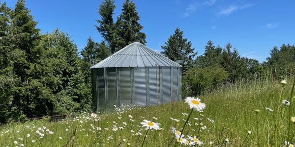 Metal silo in a grassy field with wildflowers under a clear blue sky.