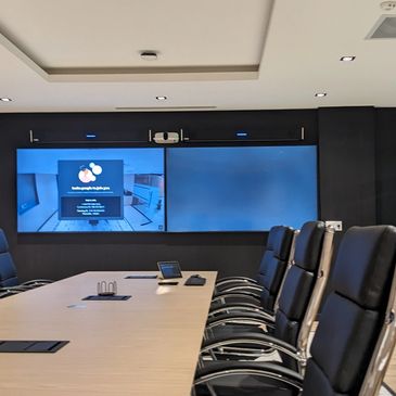 Board room table with two large video conferencing monitors and camera