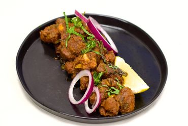 Spicy fried pakoras garnished with onion rings and lemon wedge on a black plate.