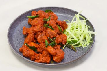 Spicy red battered chicken with green curry leaves and shredded cabbage on a gray plate.