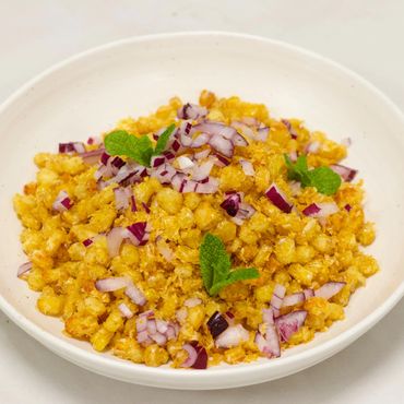 A bowl of crispy fried corn garnished with chopped red onions and mint leaves.