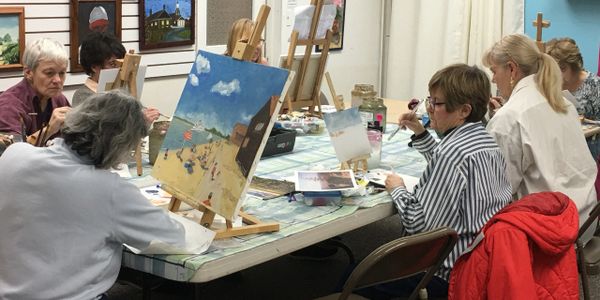 Painting art class  showing seven women seated with canvases on tabletop easels painting.