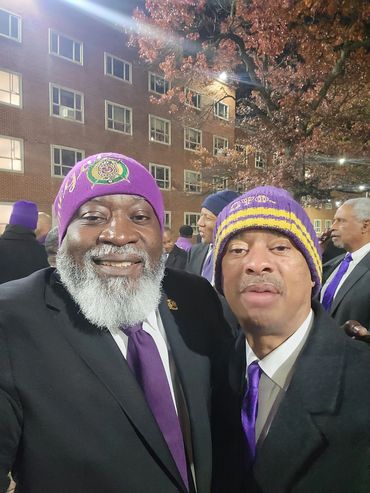 Two men in purple hats and ties smiling outdoors at night.