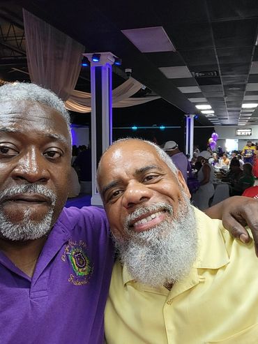 Two men smiling and posing at a lively indoor event with people in the background.