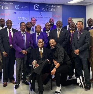 Group of men posing in formal and semi-formal attire in front of a vision board.