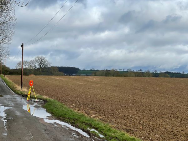 Cloudy sky over a plowed field with surveying equipment near a puddle.