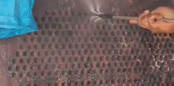 Person pressure washing a rusty perforated metal sheet.
