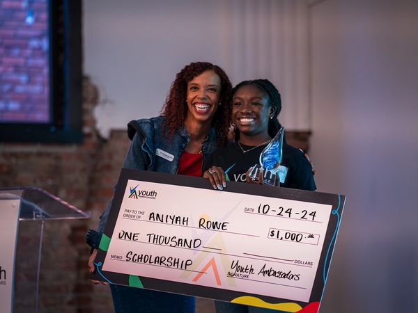 Dr. Johnston smiling with Ambassador, Aniyah as she receives her check for her award