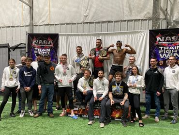Group photo of martial arts champions with medals and belts at NAGA event.