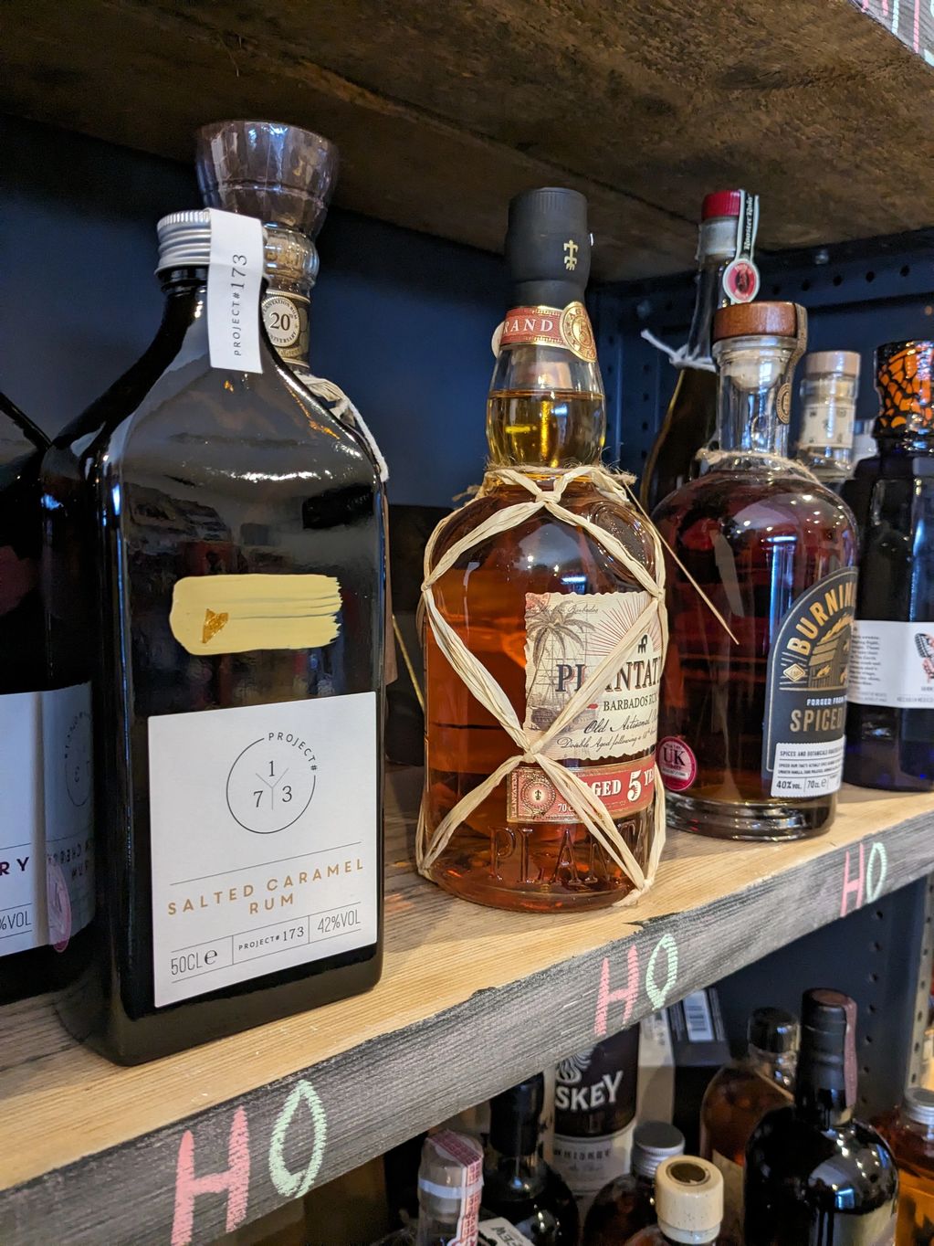 Bottles of rum and spirits on a wooden shelf with chalk markings.
