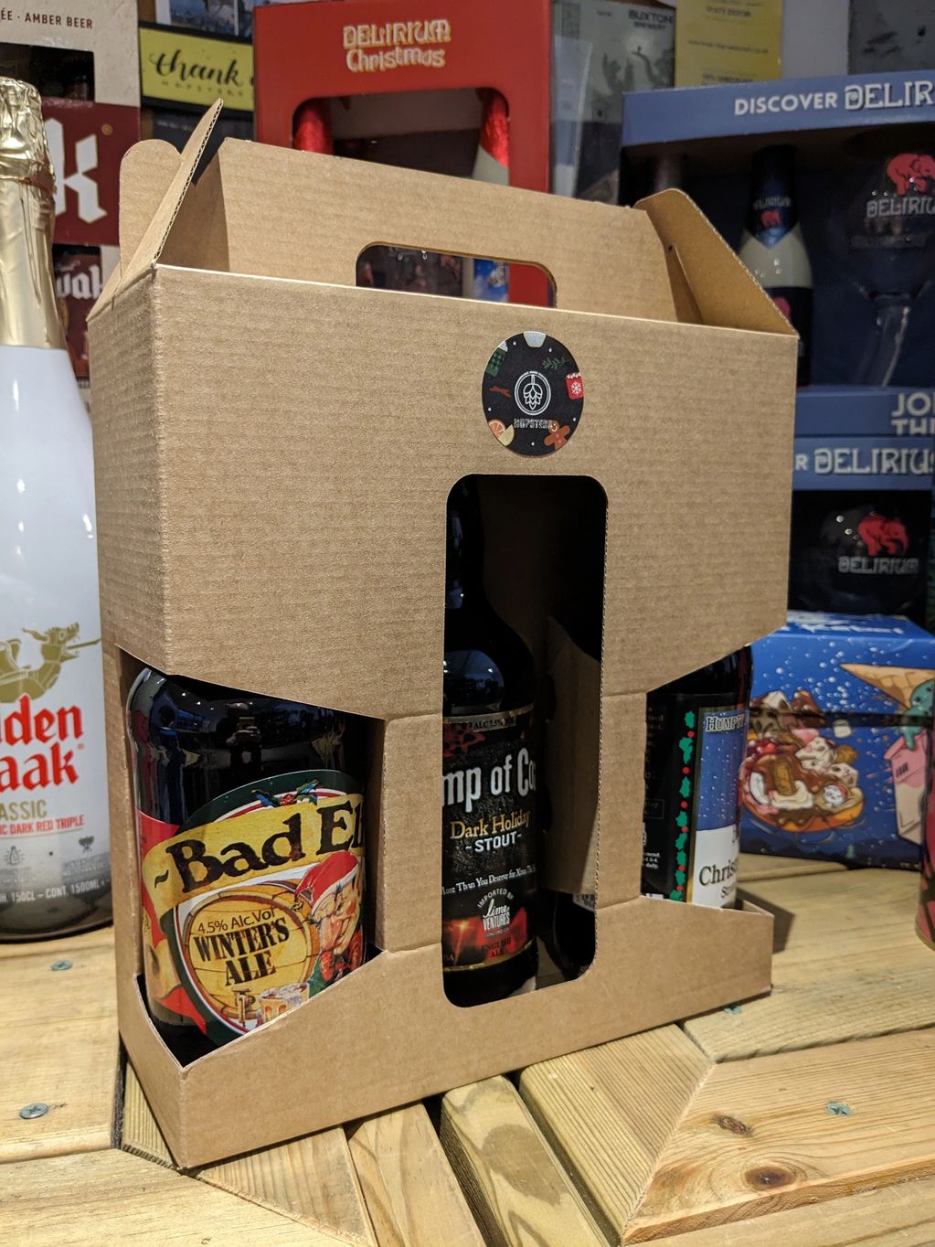 A cardboard carrier holding three craft beer bottles on a wooden surface.