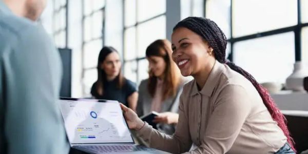 Woman smiling and presenting data on a laptop in a meeting.