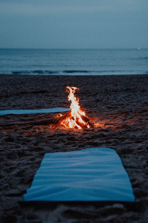 A cozy bonfire on a beach at dusk with blankets nearby.