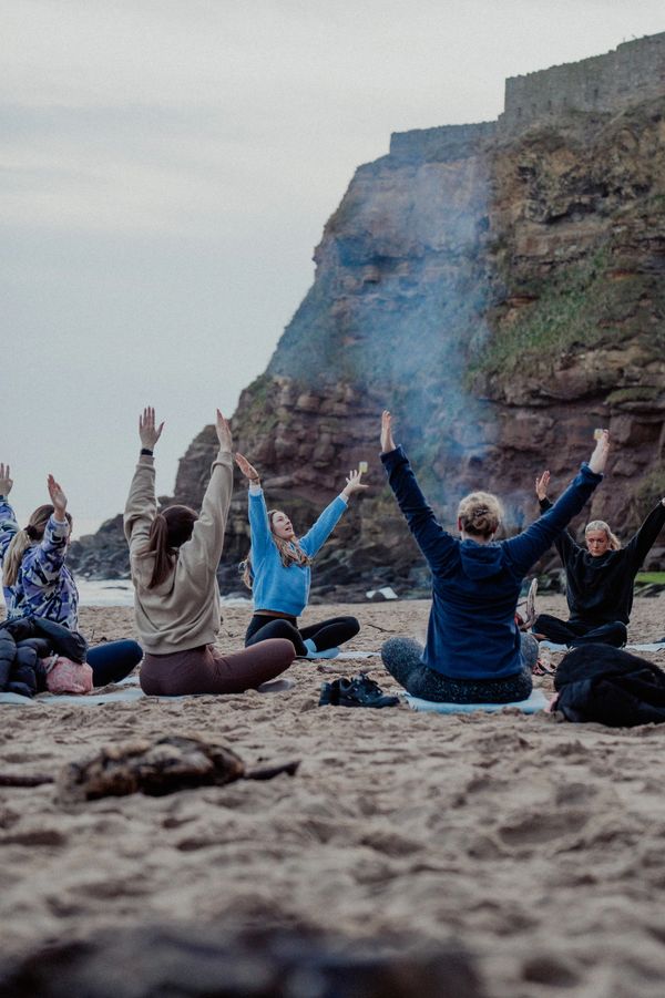 Group practicing yoga on a sandy beach with a rocky cliff backdrop.