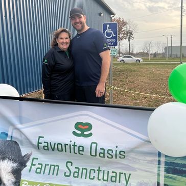 Two people smiling by a farm sanctuary sign.