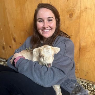 Smiling woman holding a baby goat indoors.