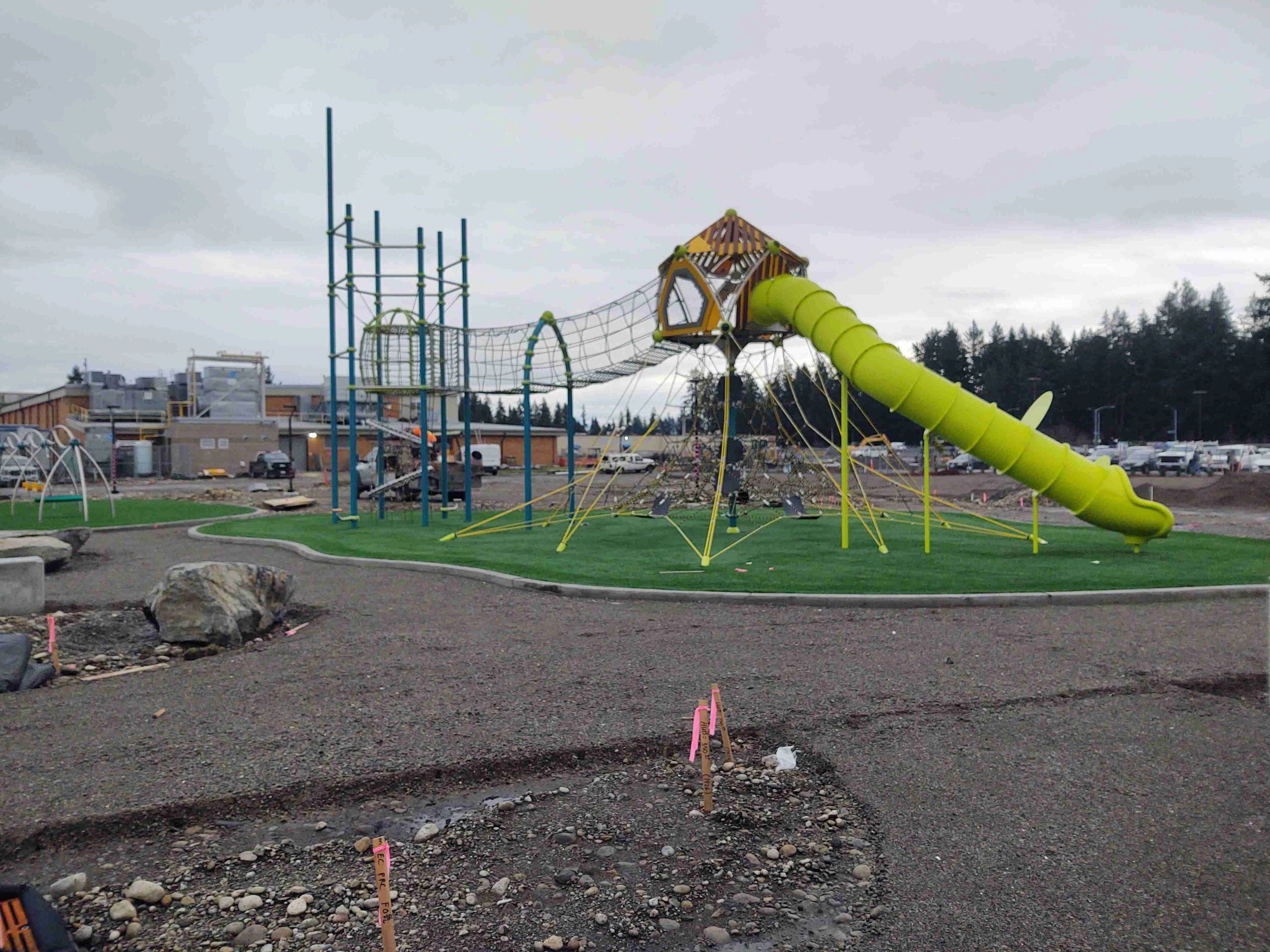 Modern playground with climbing nets and a bright green slide under a cloudy sky.