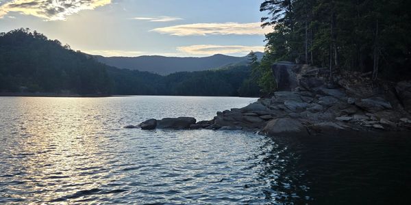 Calm lake with rocky shore and distant mountains at sunset.