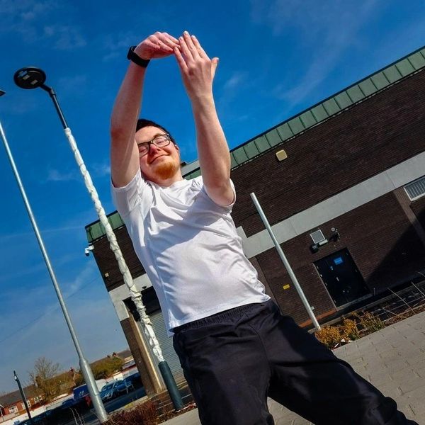 A young male adult with Down syndrome who is wearing a white T-Shirt is dancing in an urban space.