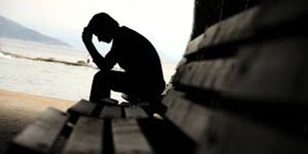 Silhouette of a person sitting on a bench with head in hands.