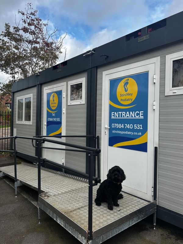 Black dog sitting on a ramp outside Stirchley Podiatry clinic.