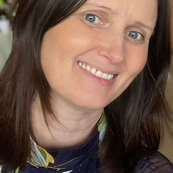 Smiling woman with blue eyes and dark hair in a floral navy dress.