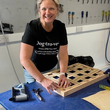 Woman smiling while working on a woven craft project in a workshop.