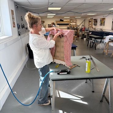 Woman upholstering furniture in a bright workshop.