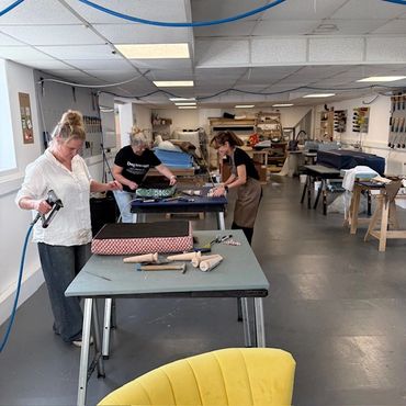 Three women working on upholstery projects in a spacious workshop.
