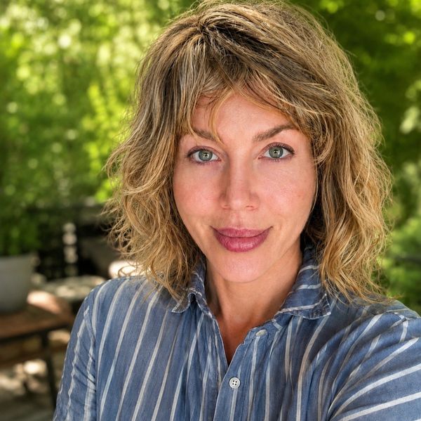 Woman with light brown curly hair in striped blue shirt smiles outside.